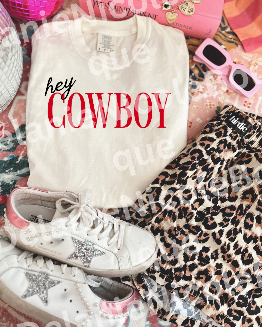White sweatshirt with 'hey COWBOY' text, white sneakers with star details, and leopard print pants on a colorful surface.